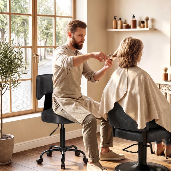 Friseur schneidet in einem hellen Salon mit Holzfenstern und Friseurstühlen die Haare einer Kundin.