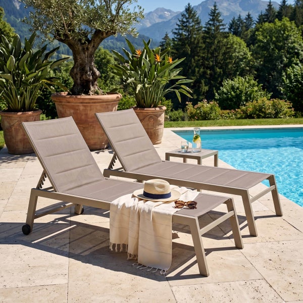 Zwei moderne Gartenliegen aus Metall und gepolstertem Textilgewebe an einem Pool auf einer Steinterrasse mit Bergblick.