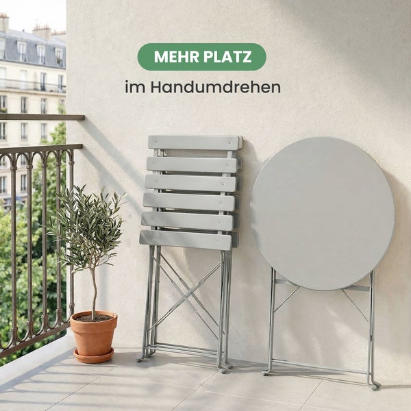 Platzsparende Balkonmöbel bestehend aus zwei zusammengeklappten Stühlen und einem runden Klapptisch auf einem hellen Balkon mit kleinem Olivenbaum.