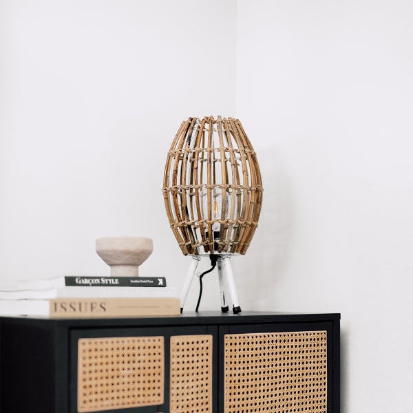 Dekorative Tischleuchte mit Rattan-Schirm auf einem schwarzen Schrank mit Rattanfront