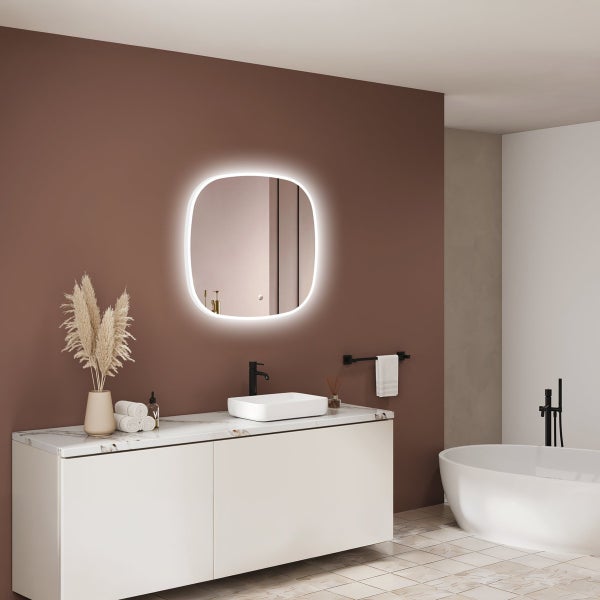 Modernes Badezimmer mit einem beleuchteten quadratischen Wandspiegel, Waschtisch mit Aufsatzwaschbecken und einer freistehenden Badewanne.