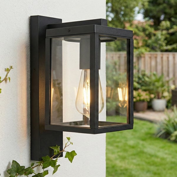 Moderne rechteckige Außenwandleuchte aus schwarzem Metall und Glas mit leuchtender LED Lampe an einer weißen Hauswand im Garten.