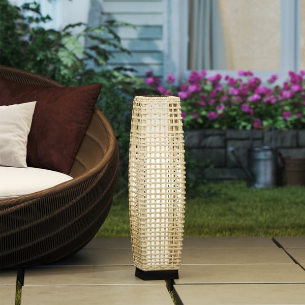 Außenstehleuchte in Rattan-Optik mit geflochtenem Schirm auf einer Terrasse neben Gartenmöbeln und Pflanzen.