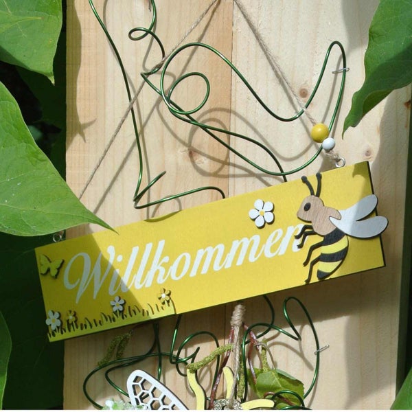 Dekoratives Holzschild mit der Aufschrift Willkommen und einem Bienenmotiv.