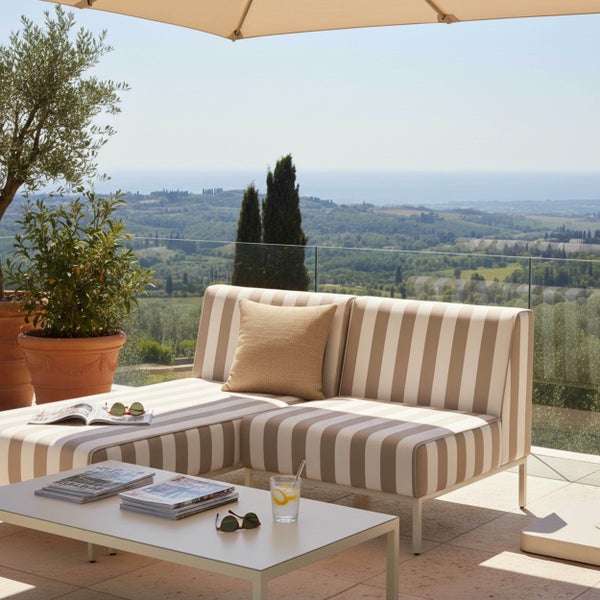Gestreifte Gartenlounge in L-Form mit passendem Couchtisch auf einer hellen Terrasse mit Blick auf eine weite Hügellandschaft.