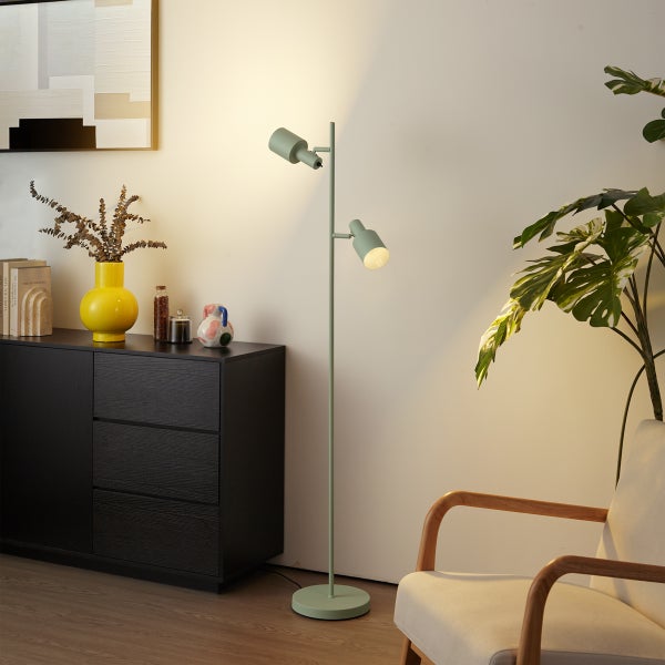 Moderne Stehleuchte mit zwei verstellbaren mintgrünen Spots in einem hellen Wohnzimmer mit Sideboard und Sessel.