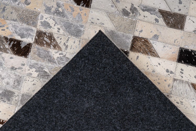 Patchwork-Teppich aus geometrischen Kuhfellstücken mit Zickzack-Nähten und einer Rückseite aus dunklem Filz.