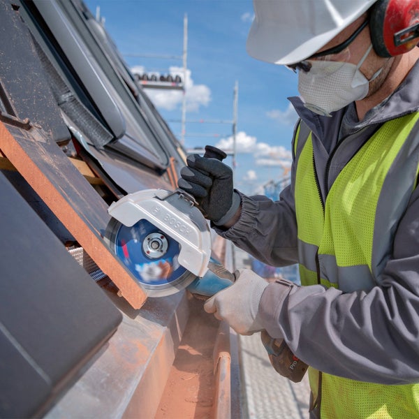 Eine Person in Schutzkleidung nutzt einen Bosch Winkelschleifer zum Schneiden von Dachziegeln auf einer Baustelle.