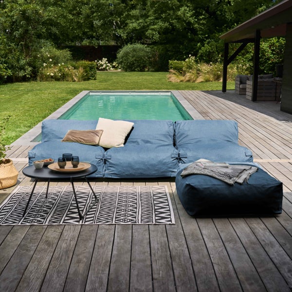 Blaue Garten-Lounge-Möbel auf einer Holzterrasse am Pool, bestehend aus modularer Couch, Hocker, Beistelltisch und einem Teppich.