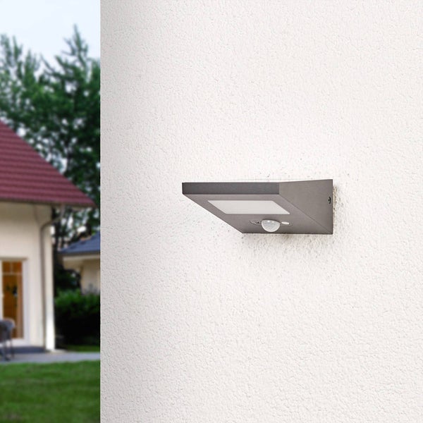 Anthrazitfarbene Solar-Außenwandleuchte mit Bewegungsmelder an einer weißen Hauswand montiert.