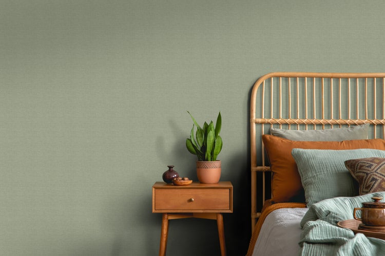 Schlafzimmer mit Rattankopfende, Nachttisch und grüner Strukturtapete.