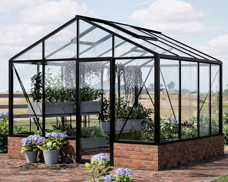 Gewächshaus mit schwarzem Aluminiumrahmen und Glasscheiben auf einem Ziegelfundament, im Inneren befinden sich verschiedene Pflanzen in Kübeln.