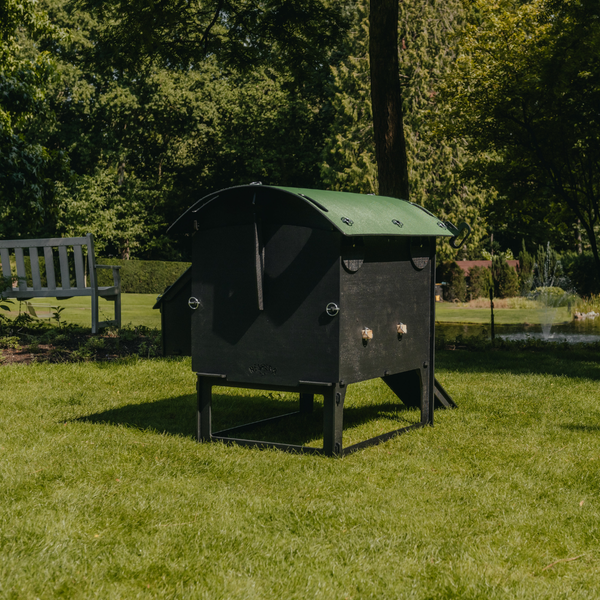Hühnerstall aus schwarzem Kunststoff mit grünem Dach im Garten auf einer Rasenfläche neben einer Holzbank.