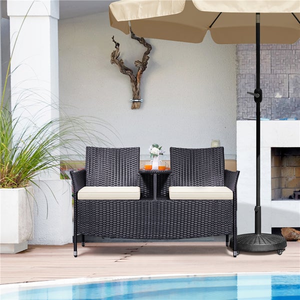 Gartenszene mit einem Doppel-Lounge-Sofa aus Rattan mit Tisch, Polster und Sonnenschirm.