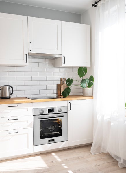 Helle Einbauküche mit weißer Front, Holz-Arbeitsplatte, U-Form Fliesenrückwand und einem integrierten Kaiser Einbaubackofen in Edelstahloptik.