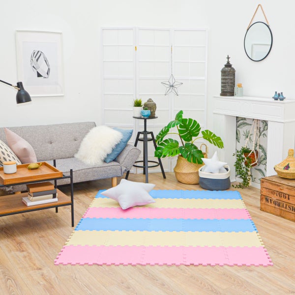 Helles Wohnzimmer mit einer bunten, gestreiften Puzzle-Spielmatte aus Schaumstoff, grauem Sofa, Sternenkissen und Zimmerpflanzen.