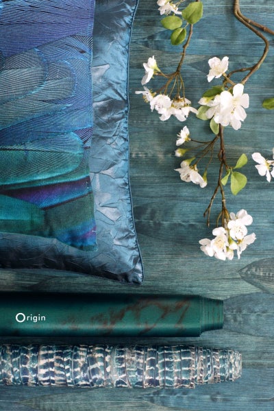 Dekoratives Arrangement mit Kissen, Tapetenrollen und blühendem Zweig auf blauem Untergrund