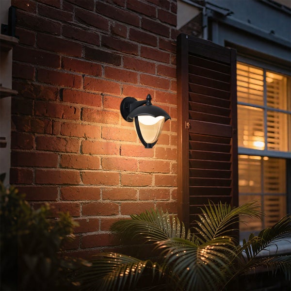 Schwarze Außenwandleuchte mit Glaseinsatz an einer Backsteinwand montiert, spendet warmes Licht.