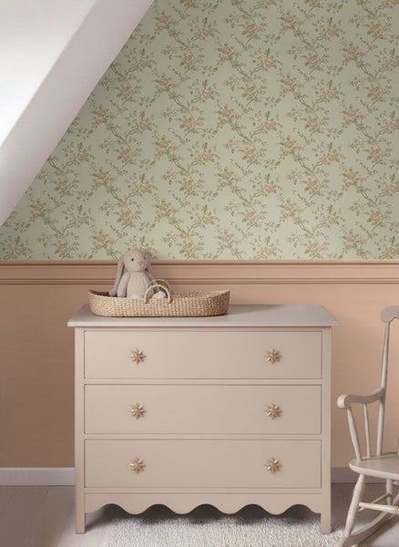 Hell gestaltetes Kinderzimmer mit floraler Vliestapete über einer Wandpaneele, einer Kommode mit Sternknöpfen und einem Weidenkorb.