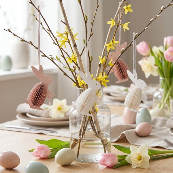 Osterstrauß in Glasvase mit hängenden Papierosterhasen und Frühlingsblumen zur Tischdekoration.