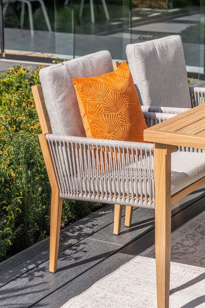 Moderner Gartenstuhl aus Holz mit Seilbespannung, grauen Polstern und orangefarbenem Zierkissen auf einer Terrasse.