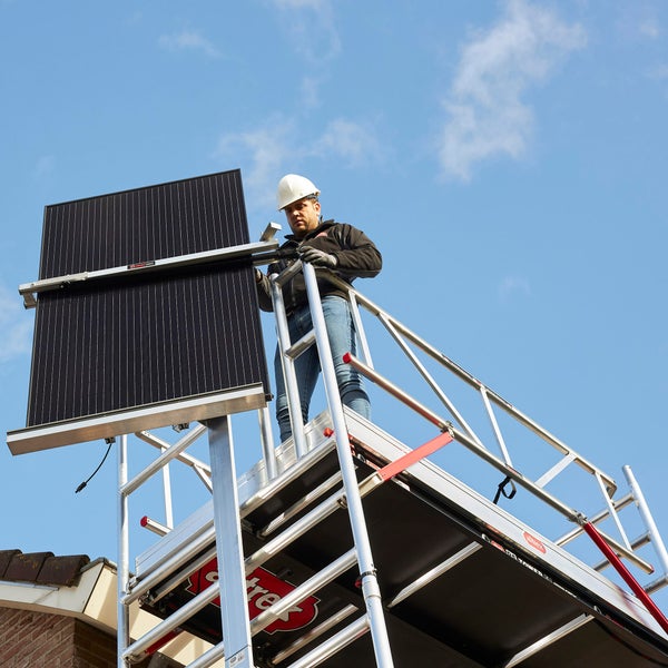 Mann montiert Solarmodul auf Gerüst vor blauem Himmel