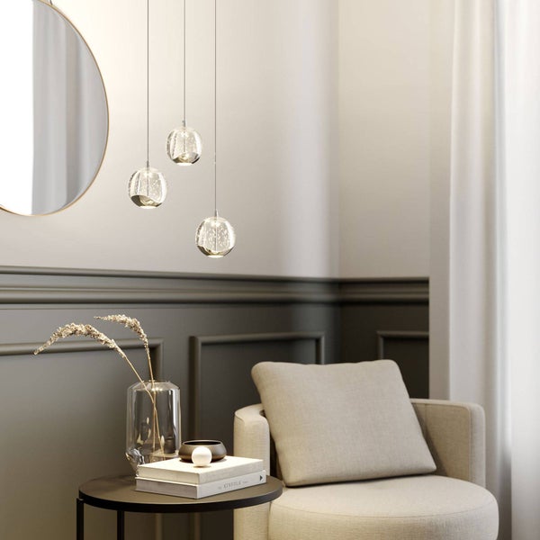 Dreiflammige Pendelleuchte mit Glaskugeln in modernem Wohnzimmer mit Sessel, Beistelltisch und Wandpaneelen.