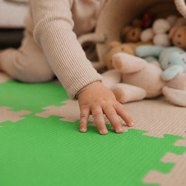 Kind spielt auf einer Puzzlematte mit strukturierter Oberfläche neben einem Korb mit Kuscheltieren