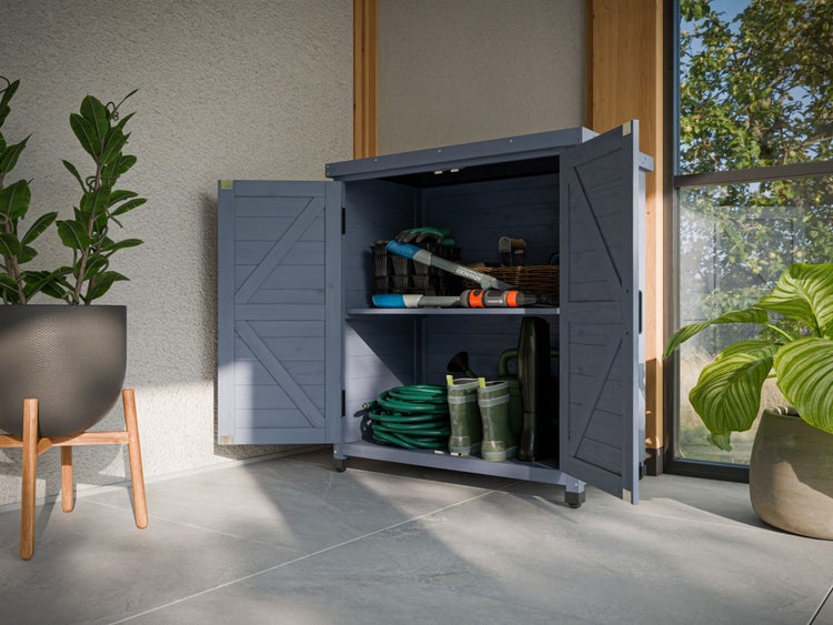 Offener Gartenschrank aus Holz auf einer Terrasse, gefüllt mit Gartengeräten wie Schlauch und Gummistiefeln neben einer Topfpflanze.