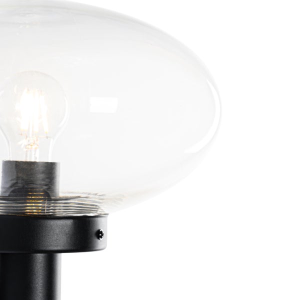 Nahaufnahme einer Außenleuchte mit transparentem Glasschirm und leuchtendem LED-Filament-Leuchtmittel auf einem schwarzen Metallsockel.