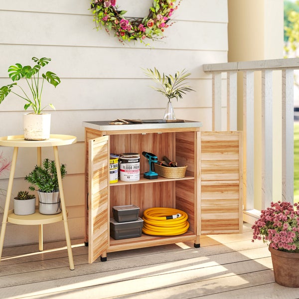 Offener Gartenschrank aus Holz auf einem Balkon mit Werkzeug, Gartenschlauch und Farbdosen, daneben ein Beistelltisch mit verschiedenen Pflanzen.