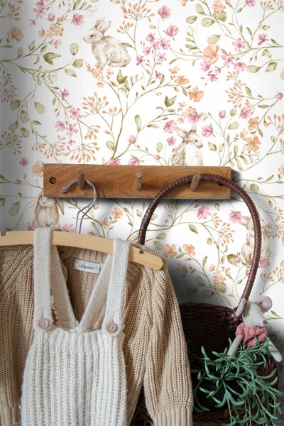 Kinderzimmer mit Tapete mit Blumen- und Hasenmuster, Kleidung an einem Holzgarderobenständer und einem Weidenkorb