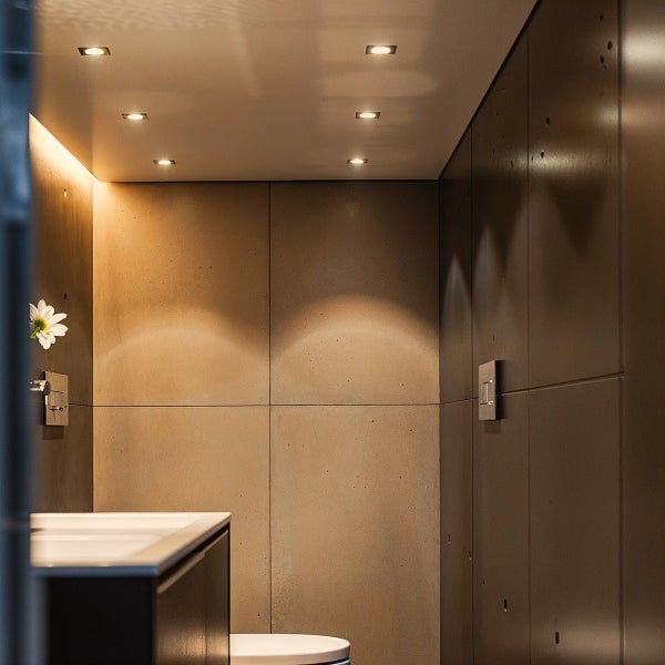 Quadratische Einbaustrahler in der Decke eines modernen Badezimmers mit Wandpaneelen in Betonoptik.
