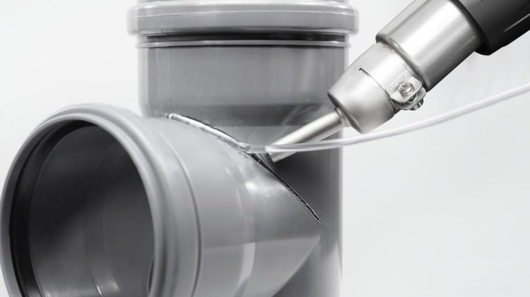 Heißluftgebläse mit Schweißdüse beim Verschweißen eines grauen Kunststoffrohrs mit Schweißdraht.