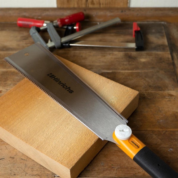 Hinrichs Japanische Zugsäge Ryoba auf einem Holzblock, im Hintergrund Schraubzwingen auf einer hölzernen Werkbank.