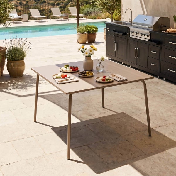 Quadratischer Gartentisch auf einer Terrasse neben einer Außenküche mit Grill und einem Pool im Hintergrund.
