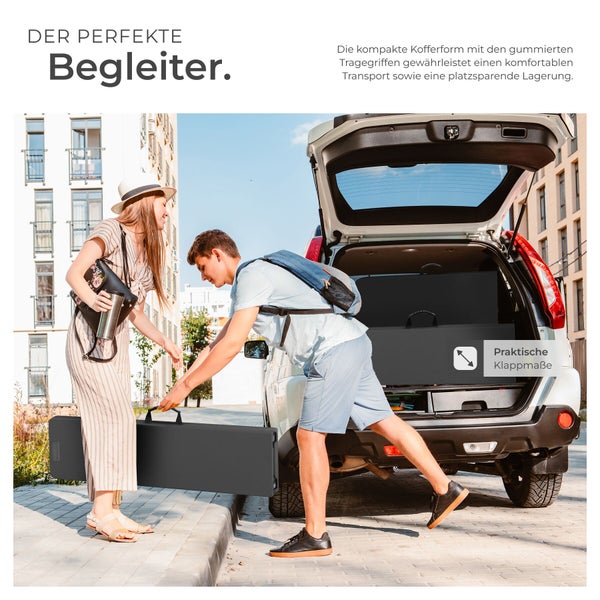 Ein Mann und eine Frau laden ein zusammengeklapptes schwarzes Solarmodul in Kofferform in den Kofferraum eines Autos.