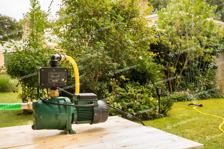 Garten mit Wasserpumpe, Steuerung und gelbem Schlauch auf einem Holztisch