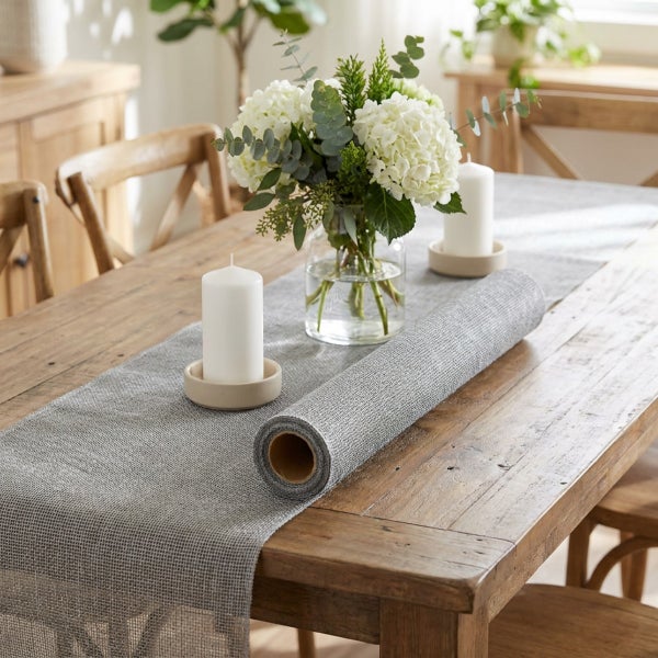 Strukturierter Tischläufer auf Rolle auf einem rustikalen Holztisch mit Blumenvase und Kerzen dekoriert.