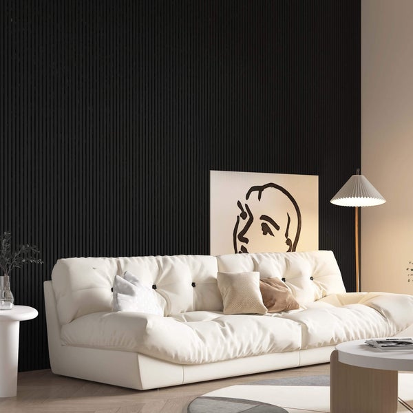 Wohnzimmer mit weichem Sofa vor einer strukturierten Wandverkleidung mit Lamellenoptik, ergänzt durch eine Stehlampe und dekorative Wandkunst.
