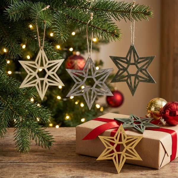 Set aus weihnachtlichen Holzsternen als Baumschmuck, hängend an einem Weihnachtsbaum mit Geschenkbox und Christbaumkugeln auf einem Holztisch.