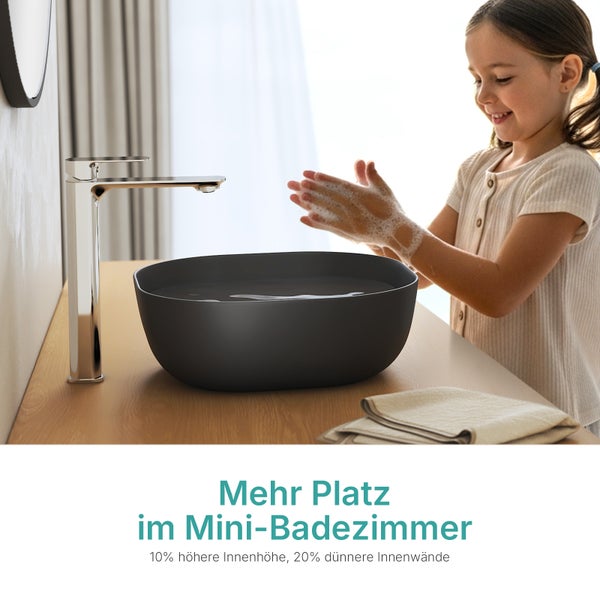 Kind wäscht Hände an einem dunklen Aufsatzwaschbecken mit hoher Chrom-Armatur auf einer Holzplatte im Badezimmer.