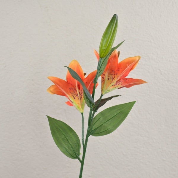 Künstliche Lilie mit orangefarbenen Blüten, einer Knospe und grünen Blättern.