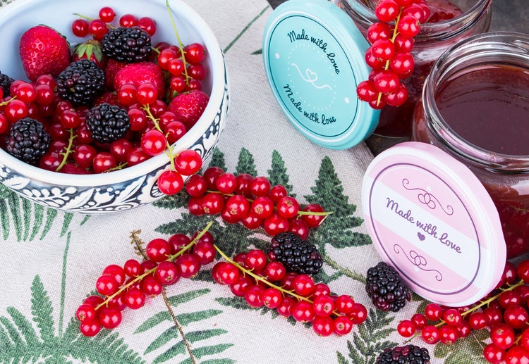 Schale mit Erdbeeren, Brombeeren und Johannisbeeren neben Marmeladengläsern mit Dekel