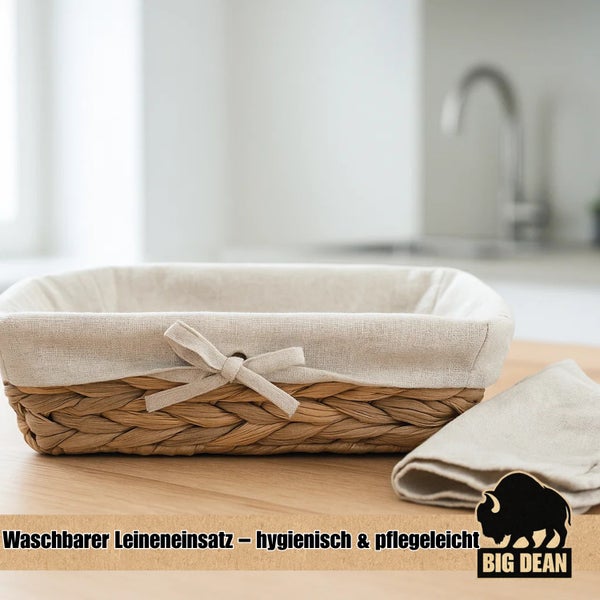 Geflochtener Brotkorb mit waschbarem Leineneinsatz und dekorativer Schleife auf einem Holztisch. Big Dean Logo.