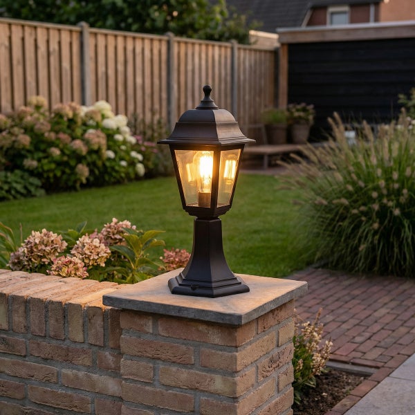 Klassische Außenstandleuchte aus Metall auf einer gemauerten Gartenmauer in einem beleuchteten Garten.