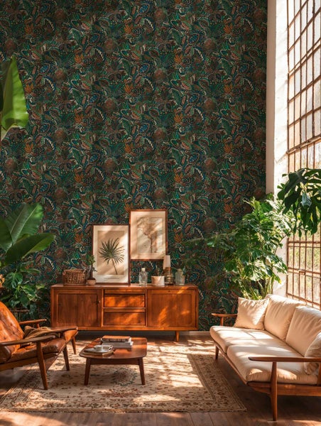 Wohnzimmer mit Vliestapete mit floralem Dschungelmotiv in dunklen Tönen, kombiniert mit Holzmöbeln im Retro Stil und zahlreichen Zimmerpflanzen.