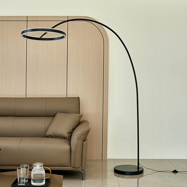 Schwarze Bogenlampe mit ringförmigem Leuchtkopf neben einem braunen Sofa in einem modern eingerichteten Wohnzimmer mit Holzpaneelen.