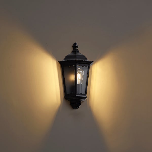 Klassische schwarze Außenwandleuchte in Laternenform mit Filament-Leuchtmittel und warmem Lichteffekt an einer Wand.