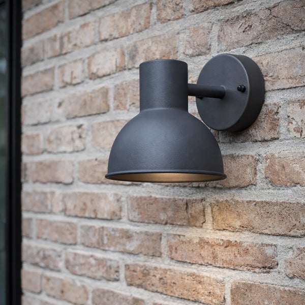 Schwarze Außenwandleuchte aus Metall mit halbkugelförmigem Schirm montiert an einer Ziegelwand.
